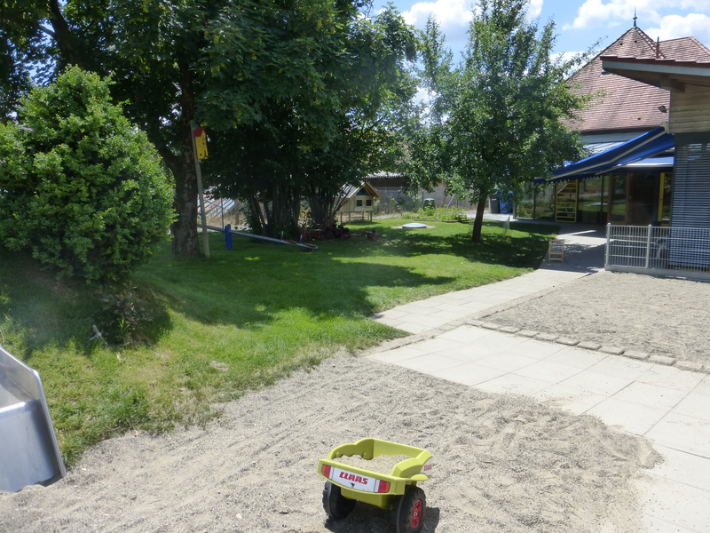 links ein Grasbereich. Rechts eine Schotterfläche auf der Spielzeug liegt. 