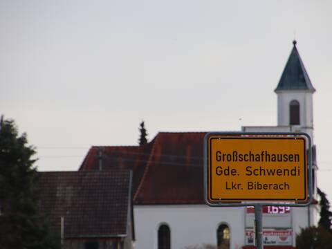 Bilde des Ortsschild von Großschafhausen von Orsenhausen kommend. Im Hintergrund ist die Kirche von Großschafhausen zu sehen.