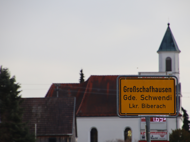 Bilde des Ortsschild von Großschafhausen von Orsenhausen kommend. Im Hintergrund ist die Kirche von Großschafhausen zu sehen.