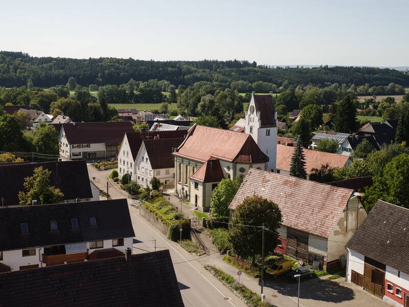Bild von erhöhter Sicht aus der Ortsverwaltung Orsenhausen mit Blick in Richtung Kirche Orsenhausen. in der Mitte eine Straße die das Bild quer kreuzt. Links und rechts davon sind Bauernhäuser und relativ zentral auf der rechten Straßenseite ist die Kirch mit dem Kirchturm zu sehen.