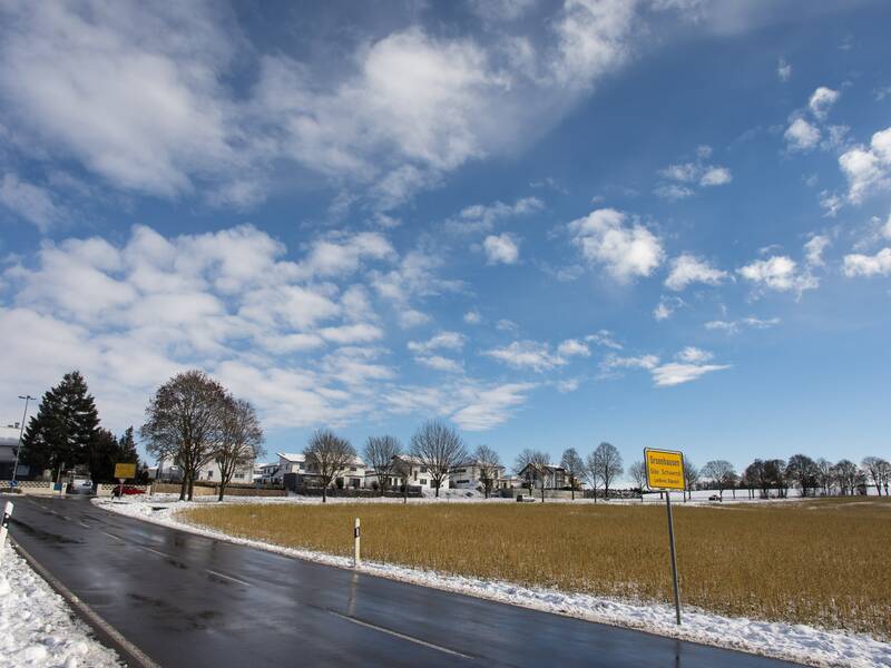 Eine Straße kreuzt das bild quer. rechts der Straße ist ein Schneebedecktes Feld zu sehen, aus dem noch grüne Pflanzen ragen. Links der straße ist eine eingeschneite Böschung zu sehen. am rechten Straßenrand steht ein gelbes Ortsschild auf dem Orsenhausen steht.