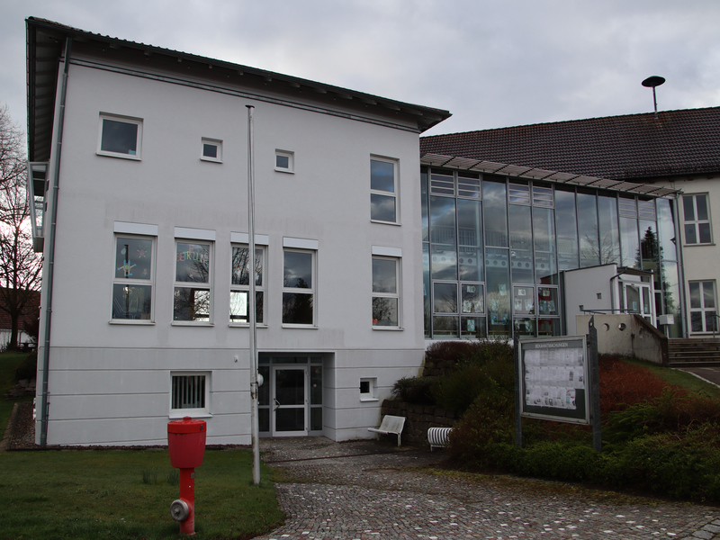 Bild der Ortsverwaltung Schönebürg im Kellergeschoss und der darüber befindlichen Grundschule Schönebürg. Links ein weiß verputztes Gebäude an das rechts ein Glasbau anschließt.Rechts endet der Glasbau wieder in ein weiß verputztes Gebäude mit vielen Fenstern.