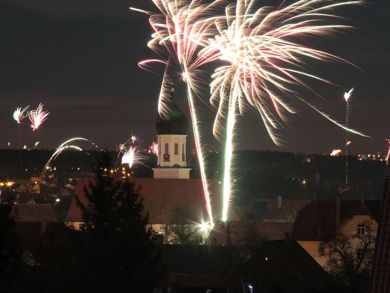 Turm der St. Stephnus Kirche in Schwendi ragt über Hausdächer, rings herum sind Feuerwerke zu sehen