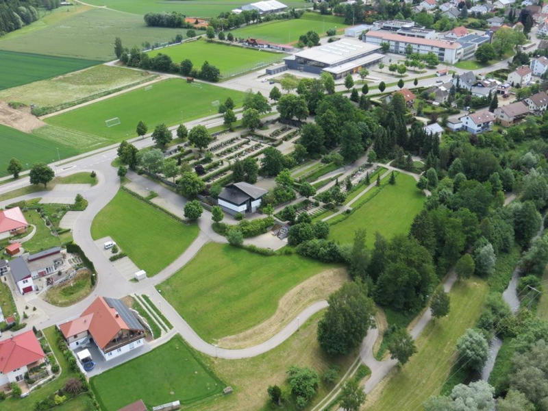 Kuftbild im Vordergrund ist ein Teil des Wohngebiets zu sehen, in der MItte der Firedhof in Schwendi mit der Aussegungshalle. Im Hintergrund ist der Schulcampus in Schwendi zu sehen