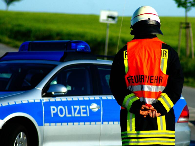 Ein Feuerwehrmann von hinten Fotofragiert vor einem Blau-silbernen Polizeifahrzeug