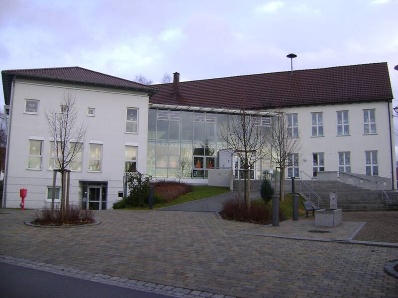 Bild der Grundschule und der Ortsverwaltung in Schönebürg. im Vordergrund ist ein gepflasterter Platz zu sehen,. Dahinter das Gebäude