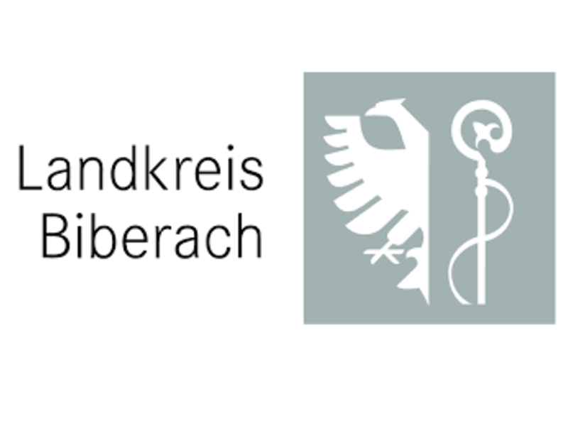 Das Logo des Landkreis Biberach. links ist der schwarze Schriftzug Landkreis Biberach auf weißem Grund zu sehen. Rechts davon auf grauem quadratischem Grund, in weiß in der linken Hälfte ein Adler und in der rechten Hälfte ein Bischofsstab.