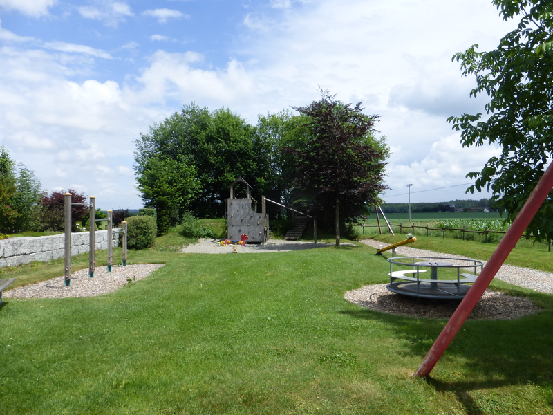 In der Mitte eine Wiese. links und rechts im Bild auf der Wiese sind mehrer Spielgeräte zu sehen.