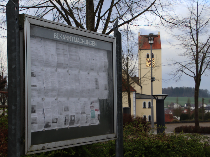 Bekanntmachungstafel vor Bäumen und einem Kirchturm (Schönebürg)